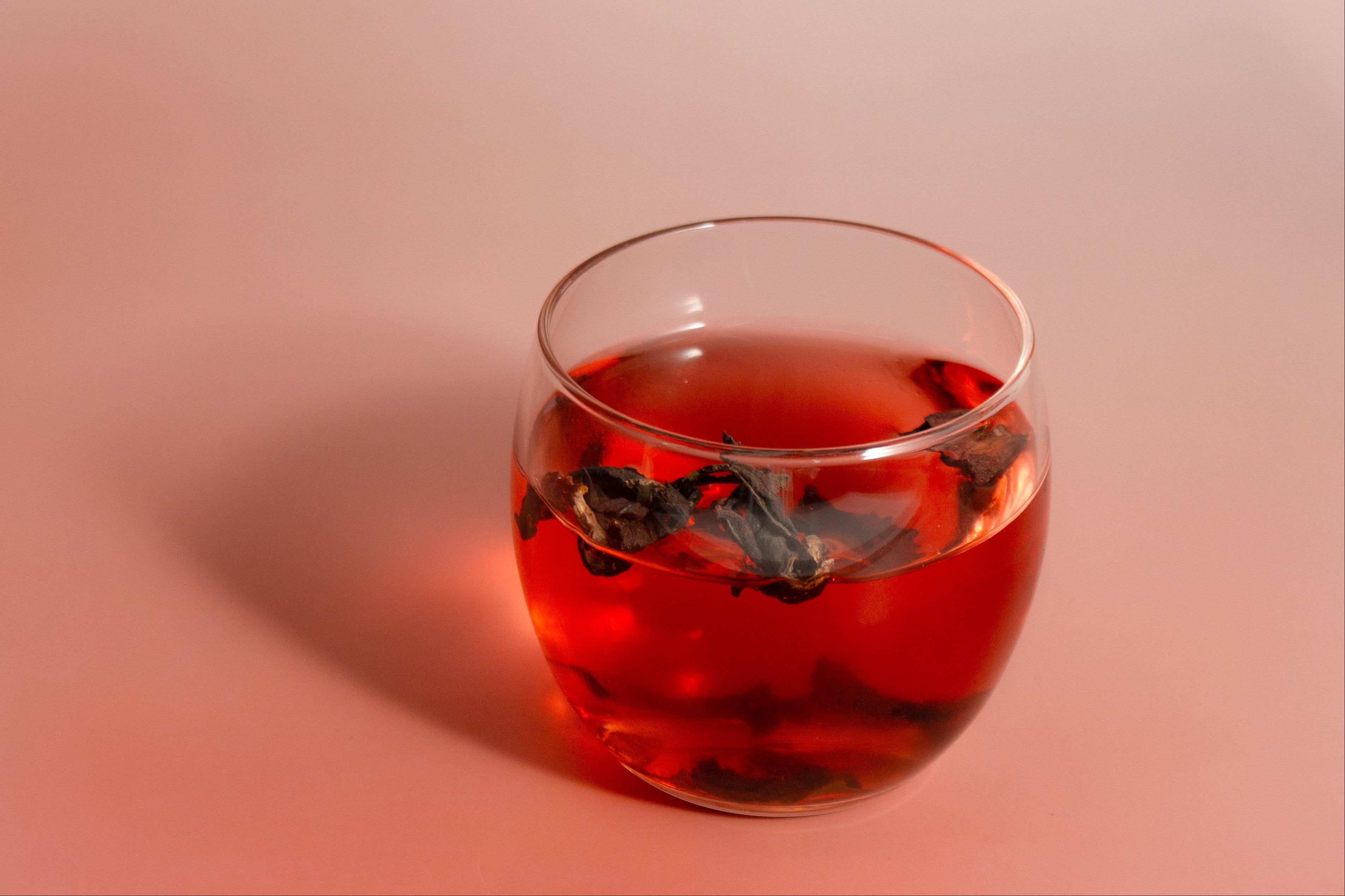 Glass of red liquid with floating herbs on a pink background